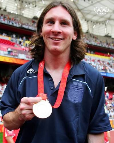 Lionel Messi smiling and holding his Olympic gold medal in Beijing
