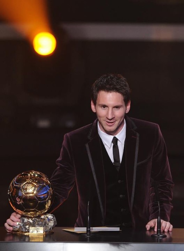 Lionel Messi in a velvet jacket at the podium beside the Ballon d'Or