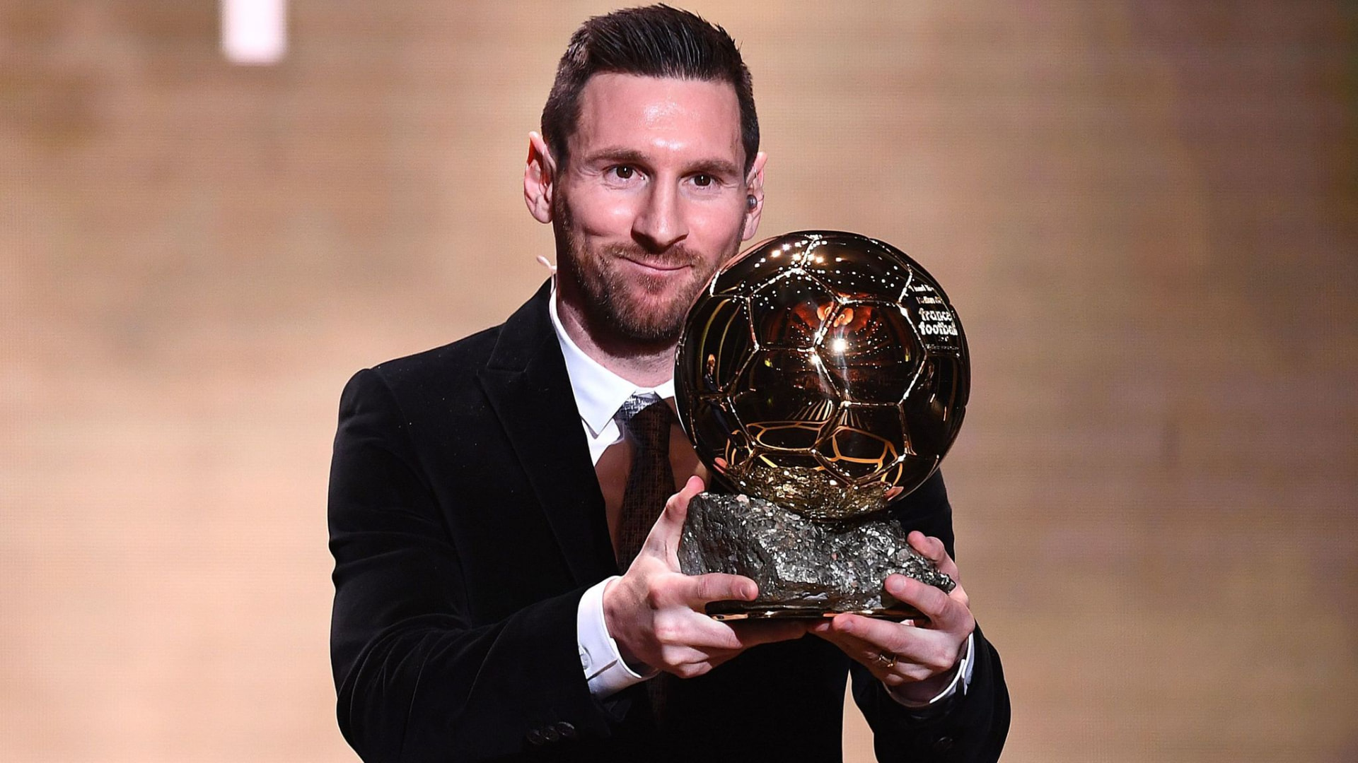 Lionel Messi in a velvet suit holding up his sixth Ballon d'Or