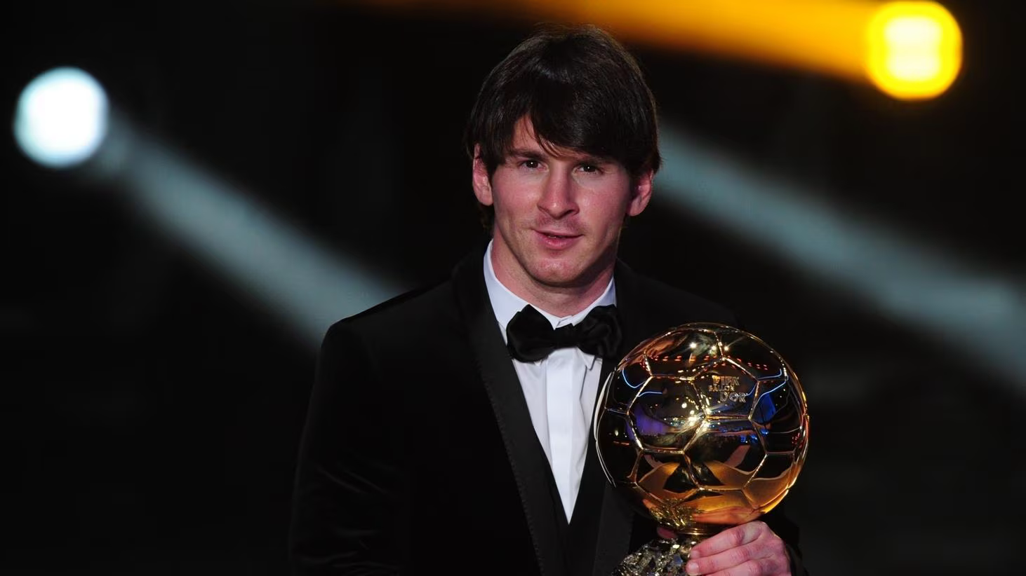 Lionel Messi in a tuxedo holding the Ballon d'Or on stage