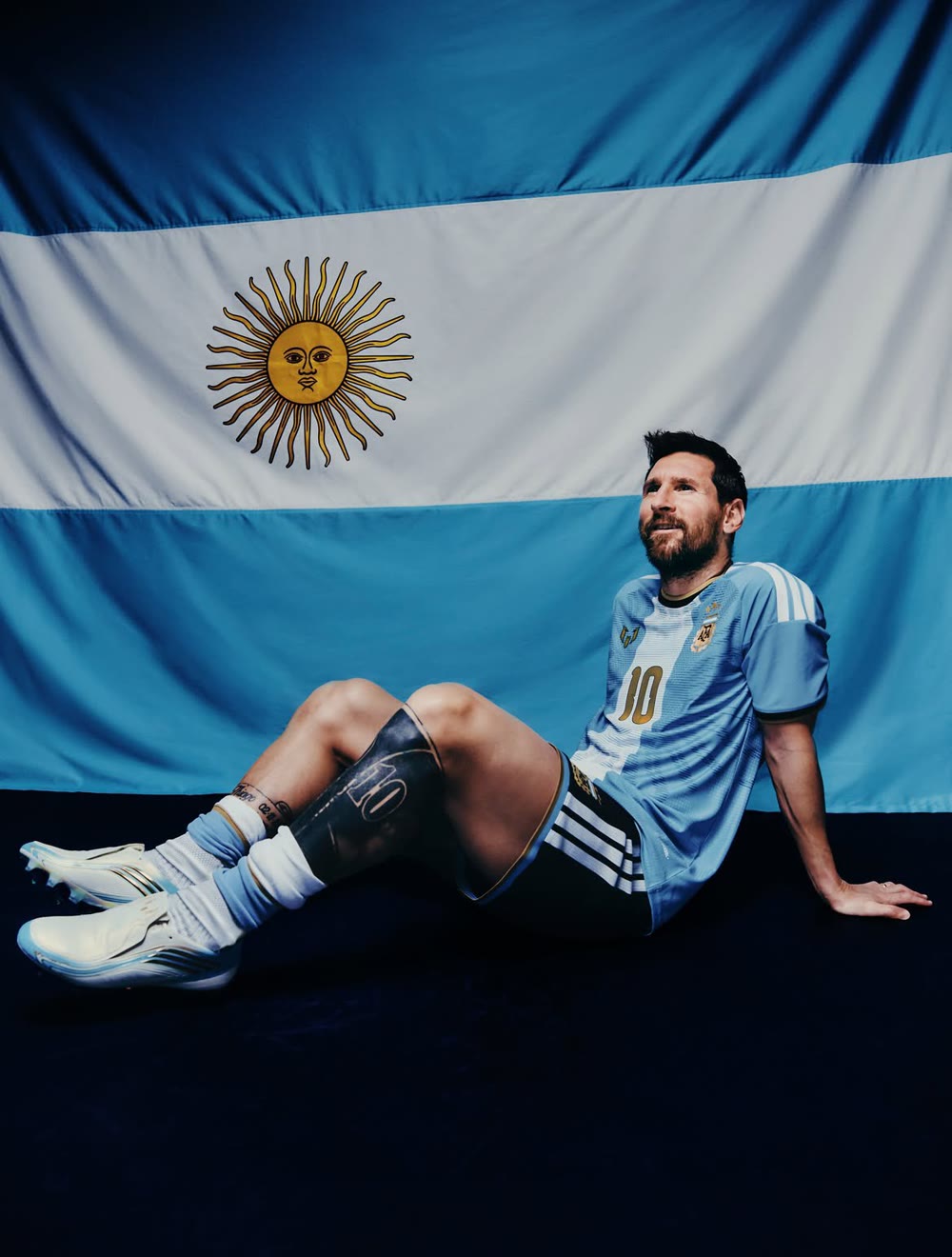 Lionel Messi in the Argentina shirt sitting in front of a large Argentina flag